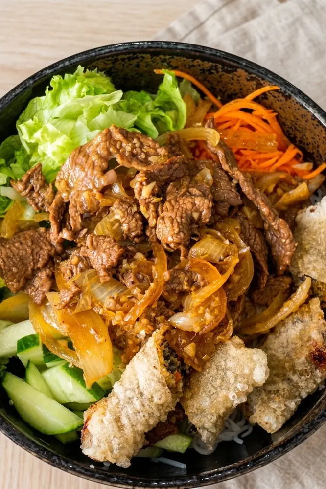 Bol de bœuf sauté, porc croustillant, salade et crudités